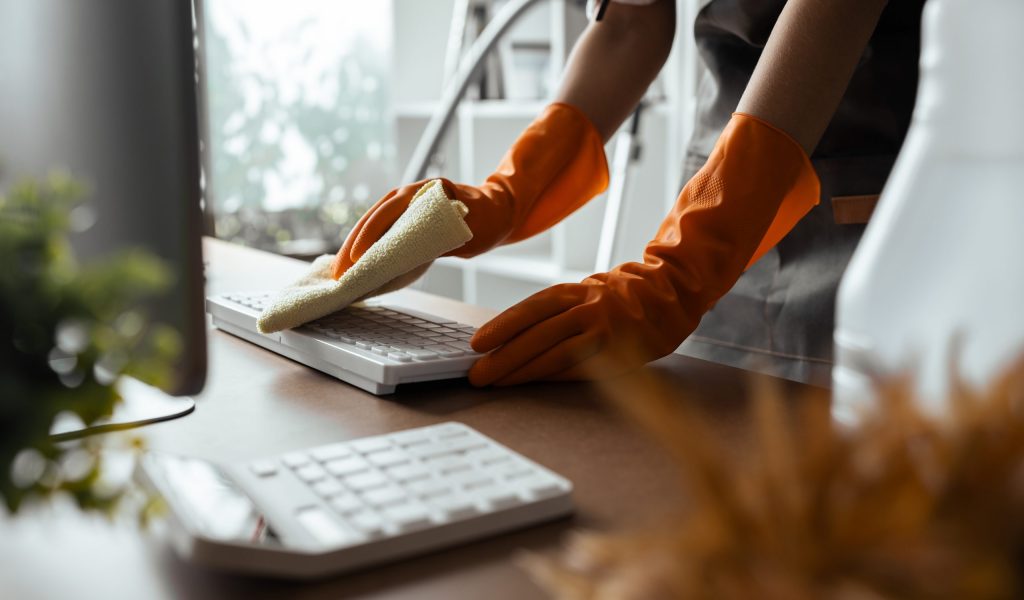Woman maid cleaning and wiping the keyboard with microfiber cloth at desk in office.